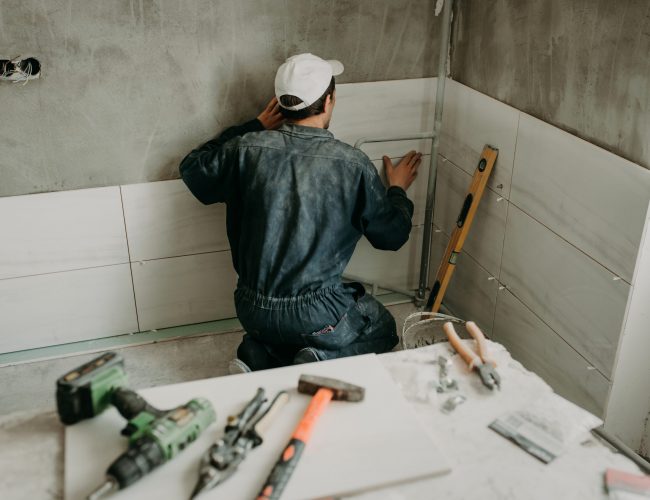 Worker repairman puts large ceramic tiles on the walls in the room